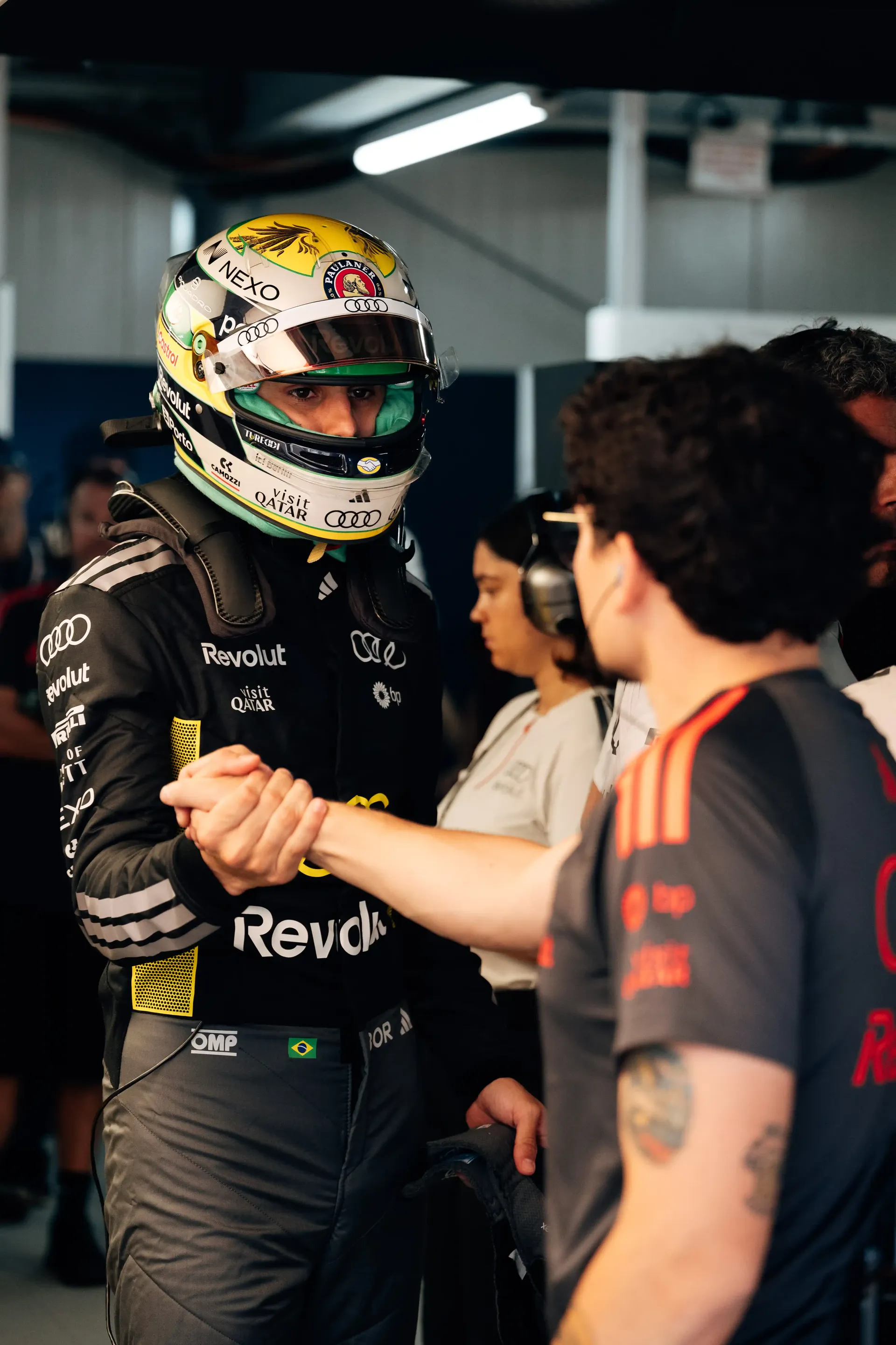 Gabriel Bortoleto  in his race helmet speaks with Audi Revolut F1® Team mechanic inside the garage.