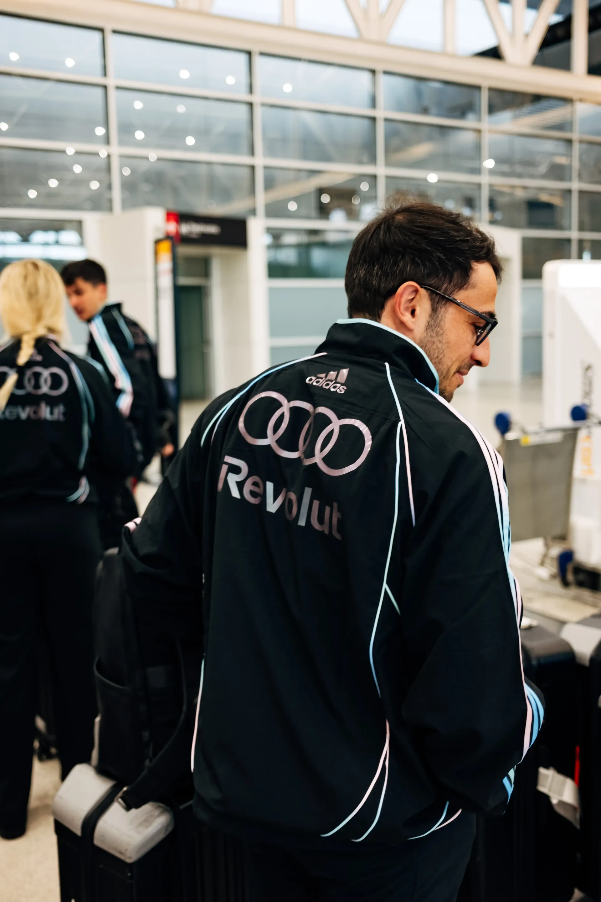 Backshot of Audi Revolut F1®Team crew member walking through terminal corridor in the new Miami collection tracksuit.